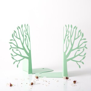 May include: A pair of green metal bookends shaped like trees. The bookends are on a white surface with white flower petals scattered around them.