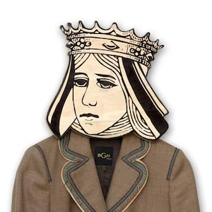 May include: A brown blazer with a black and white illustration of a queen wearing a crown. The blazer has a decorative trim around the collar and pockets. The illustration is on a wooden plaque.