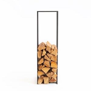 Front view of a tall minimalist black metal firewood rack neatly filled with stacked logs, showing modern Scandinavian indoor log storage design.