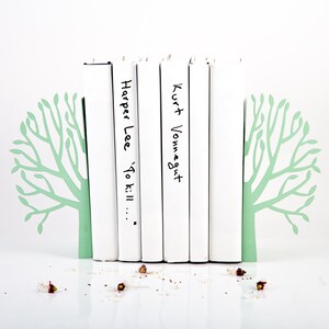 May include: White bookends shaped like trees with green leaves holding up a stack of books. The books have the titles "Harper Lee 'To Kill..." and "Kurt Vonnegut" written on them.