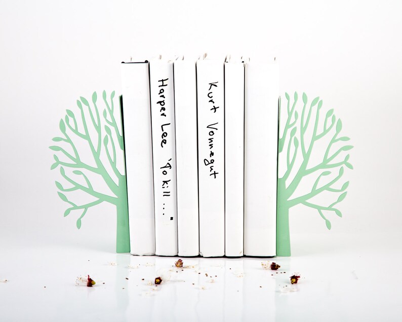 May include: White bookends shaped like trees with green leaves holding up a stack of books. The books have the titles "Harper Lee 'To Kill..." and "Kurt Vonnegut" written on them.