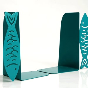 May include: Teal blue metal bookends shaped like fish. The fish have a white outline and a wavy pattern.