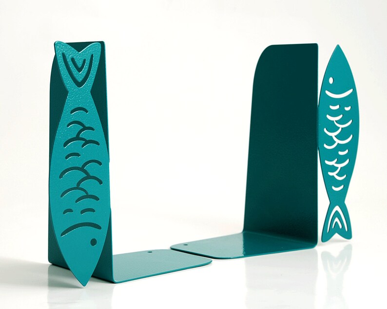 May include: Teal blue metal bookends shaped like fish. The fish have a white outline and a wavy pattern.