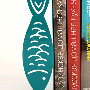 May include: Teal blue metal fish bookends holding up three books with titles in Russian and Georgian. The titles are "Грузинская домашняя кухня", "Русская домашняя кухня", and "ИМПЕрия КУХНИ".