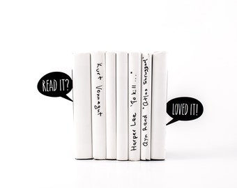 May include: A stack of white books with black handwritten titles. The titles are "READ IT?", "Kurt Vonnegut", "Harper Lee 'To Kill...", "Ayn Rand 'Atlas Shrugged", and "LOVED IT!"