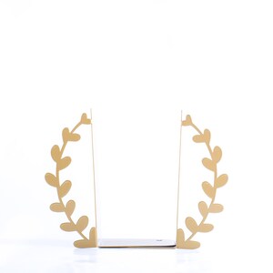 May include: Gold metal bookends shaped like a leafy wreath. The bookends are open and ready to hold books.