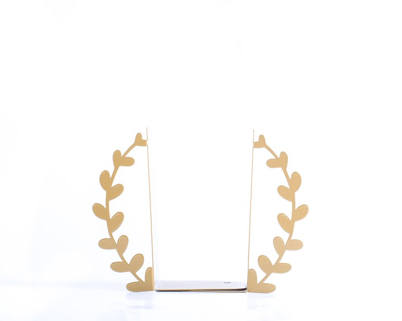 May include: Gold metal bookends shaped like a leafy wreath. The bookends are open and ready to hold books.