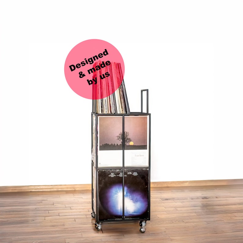 May include: Black metal record storage cart with wheels, filled with vinyl records. The cart has four shelves and a pink circle sticker that says "Designed & made by us".