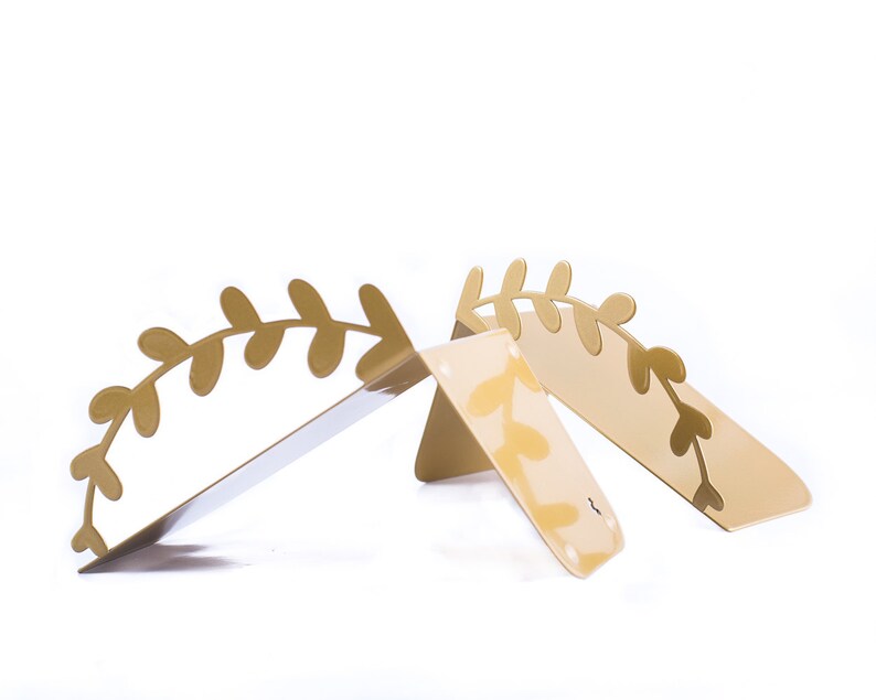 May include: Two gold metal bookends shaped like a leafy branch. The bookends are angled to create a V-shape.