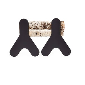 Puede incluir: Dos ganchos de metal negro en forma de V, montados en una pieza de madera de abedul.
