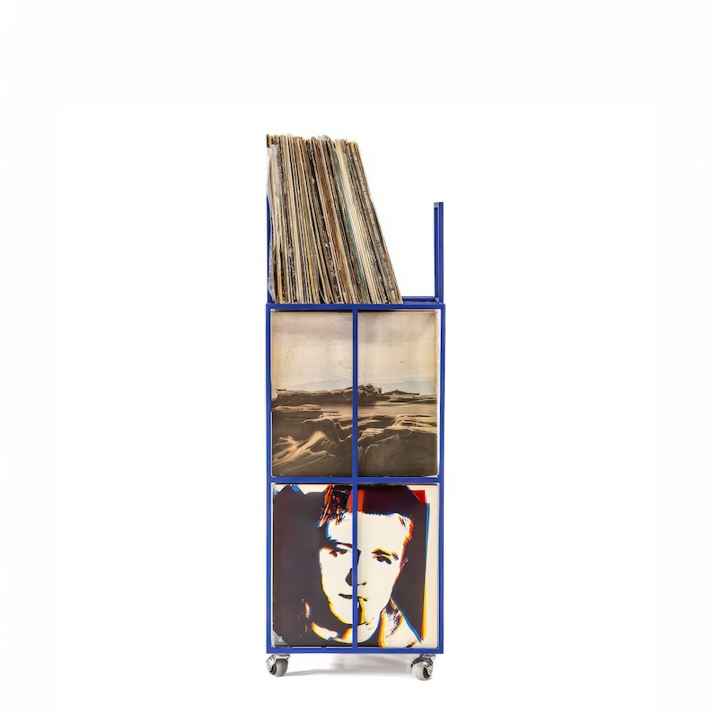 May include: A blue metal record storage unit with wheels. The unit has four shelves, each filled with vinyl records. The records have various album covers, including a landscape scene and a portrait of a person.