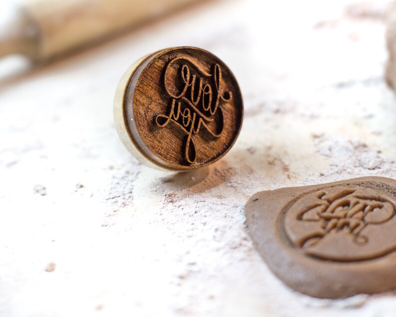 May include: A wooden stamp with the words "Love you" carved into it. The stamp is on a white surface with a brown cookie that has been stamped with the same design.