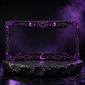 May include: A rectangular black license plate frame featuring a purple graphic design of a cat face at the top center, a crescent moon at the bottom center, and intricate purple rose and vine patterns along the entire border of the frame.