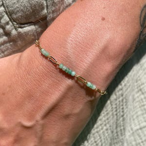 Peut inclure: Un bracelet à chaîne doré délicat orné de petites perles rondes en pierre précieuse vert clair intercalées le long des maillons. Le bracelet se compose de maillons métalliques ovales allongés alternant avec des sections de minuscules pierres lisses.