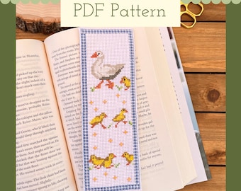 May include: A cross-stitch pattern for a bookmark featuring a white goose with four yellow chicks. The pattern is on a white background with blue and white gingham trim. The text "PDF Pattern" is at the top of the bookmark.