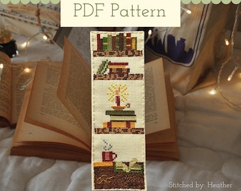May include: A rectangular cross-stitch bookmark on cream fabric featuring four stacked designs: a row of books, a small house, a stack of books with a lit candle, and a red mug next to an open book. The text PDF Pattern is at the top.