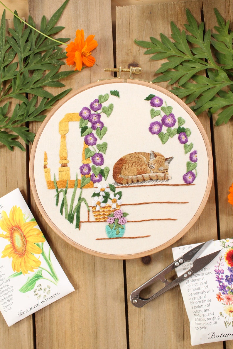 an embroidery of a sleeping cat on a front porch surrounded by purple morning glory flowers