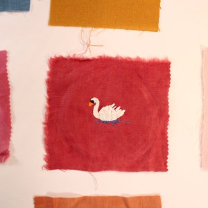 Red linen fabric patch with an embroidered swan on it.