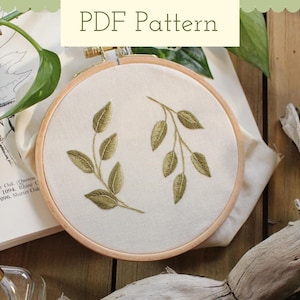 May include: A PDF pattern for embroidery featuring two green leafy branches on a white background. The pattern is displayed in a wooden embroidery hoop.