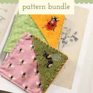 Könnte beinhalten: Handgefertigte Stoff-Lesezeichen mit gestickten Insektenmotiven. Die Lesezeichen zeigen einen Marienkäfer, eine Hummel und Bienen. Der Text "pattern bundle" steht oben. Die Lesezeichen liegen auf einem offenen Buch.