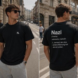 Könnte beinhalten: Ein schwarzes Kurzarm-T-Shirt mit dem Buchstaben N. auf der linken Brustseite. Auf der Rückseite ist das Wort Nazi, die phonetische Aussprache, die grammatikalische Einordnung und eine Definition in deutschem Text in Weiß gedruckt.