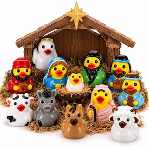 Puede incluir: Un set de belén con doce patitos de goma dispuestos frente a una estructura de establo de madera con una estrella dorada en la parte superior. Las figuras incluyen personajes con túnicas coloridas, un patito bebé en un pesebre y animales.