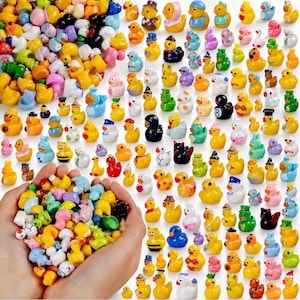 May include: A large collection of miniature rubber ducks in various colors, patterns, and themes, including some wearing hats, costumes, or featuring sports designs, with a handful held in two hands in the foreground.
