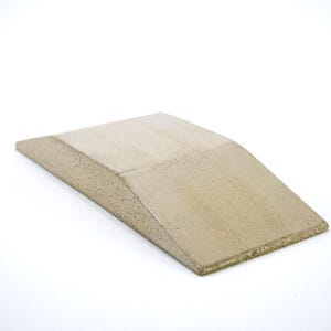 May include: A beige, wedge-shaped block with a smooth, slightly textured surface. The object features a flat, rectangular top section that slopes downward at an angle toward the front edge, creating a low-profile, ramp-like form with visible granular details.