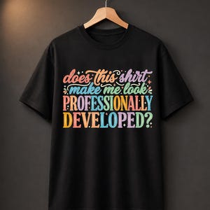 May include: A black short-sleeved t-shirt featuring the colorful text "does this shirt make me look PROFESSIONALLY DEVELOPED?" in a variety of pastel and bright hues, including pink, blue, orange, and purple, displayed on the front chest area.
