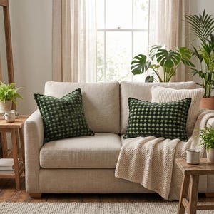 Könnte beinhalten: Ein beiges Polstersofa mit zwei quadratischen und rechteckigen Zierkissen mit einem geometrischen Rautenmuster in Dunkelgrün und Hellgrün. Eine cremefarbene, strukturierte Wohndecke liegt über der rechten Seite der Sofakissen.