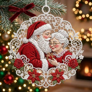 Può includere: Un addobbo natalizio circolare in pizzo bianco con una scena ricamata di Babbo Natale che bacia la Mamma Natale sulla fronte. Il design include rose rosse, stelle di Natale e un piccolo regalo rosso. Un fiocco di velluto rosso è fissato in alto.