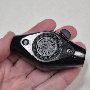 May include: A black, diamond-shaped electrical cord switch with a textured circular center. The center features the embossed text 1A 250V, UND. LAB. INSP., and 3A 125V. It includes two metal screws and a small black sliding toggle switch on the side.