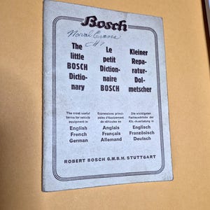 May include: A vintage booklet with the Bosch logo and the text "The little BOSCH Dictionary" in English, French, and German. The booklet also lists vehicle equipment terms in multiple languages. The booklet is on a yellow background.