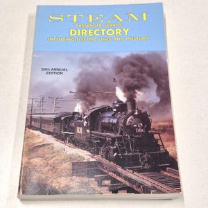 May include: A vintage book titled "STEAM PASSENGER SERVICE DIRECTORY" with a blue cover and a picture of a black steam train. The cover also includes the text "INCLUDING ELECTRIC LINES AND MUSEUMS" and "24th ANNUAL EDITION".