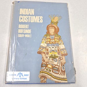 May include: A light blue hardcover book titled Indian Costumes by Robert Hofsinde Gray-Wolf. The cover features an illustration of a person in a patterned robe and headdress. A white Morrow Eagle Library Edition sticker is at the bottom left.