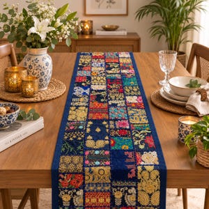 Op de afbeelding: Een rechthoekige tafelloper met een patchworkontwerp van diverse stoffen vierkanten in diepblauw, goud, rood en groen. De loper is versierd met ingewikkeld borduurwerk, accenten van metaaldraad en bloemmotieven, afgewerkt met een effen blauwe rand.