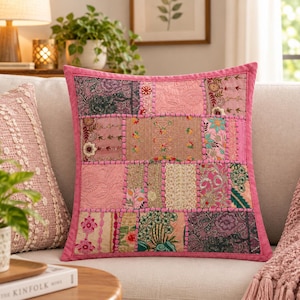 May include: A square throw pillow featuring a patchwork design of various pink, gold, and green fabric panels. The surface is decorated with intricate embroidery, floral patterns, and metallic thread accents, all framed by a solid pink border.