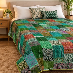 Puede incluir: Una colcha de patchwork que presenta una variedad de paneles de tela cuadrados en tonos verde, azul verdoso y óxido con patrones florales y geométricos. La colcha está cosida con líneas de hilo blanco visibles y tiene un borde verde sólido.