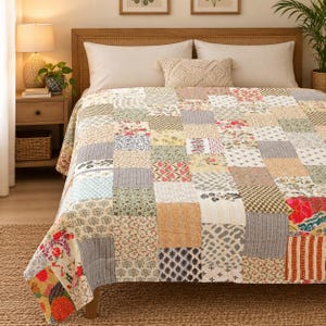 Könnte beinhalten: Eine Patchwork-Tagesdecke mit einer Vielzahl quadratischer Stoffblöcke in verschiedenen Blumen-, geometrischen und Streifenmustern in gedeckten Beige-, Grün-, Blau- und Rottönen, die über einem Bett mit zwei weißen Kissen und einem strukturierten Kissen liegt.