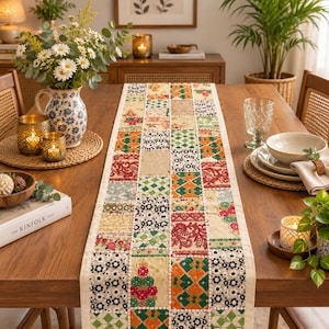 Puede incluir: Un camino de mesa rectangular con un diseño de patchwork de varios cuadrados de tela bordados en tonos rojo, verde, naranja y crema. El camino muestra intrincados patrones florales, geométricos y de puntos cosidos con hilo blanco.