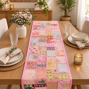 Peut inclure: Un chemin de table rectangulaire présentant un motif patchwork composé de divers carrés de tissu dans des tons de rose, jaune et vert. Le chemin est bordé d'une bordure en tissu rose uni et affiche des broderies et des motifs floraux complexes.