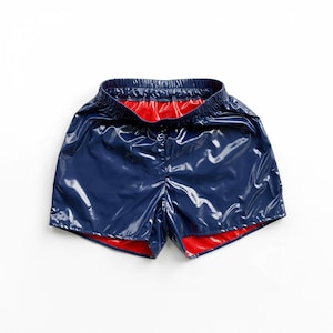 Könnte beinhalten: Glänzende marineblaue Shorts mit einer spiegelnden Oberfläche und einem leuchtend roten Innenfutter. Die Shorts verfügen über einen elastischen Bund und einen kurzen, sportlichen Schnitt mit einer glatten, vinylartigen Textur auf der Außenseite.