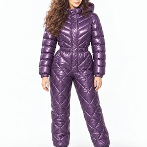 Op de afbeelding: Een glanzende paarse gewatteerde jumpsuit uit één stuk met een hoge kraag, ritssluiting aan de voorzijde, lange mouwen met elastische boorden en een getailleerde taille. Het bovenstuk heeft een chevronpatroon en de broek een ruitpatroon.