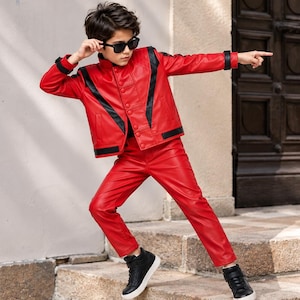 Può includere: Un completo composto da giacca e pantaloni in ecopelle rosso brillante con inserti neri a forma di V sul petto, polsini neri e dettagli neri sull'orlo. L'outfit è abbinato a scarpe da ginnastica alte nere e occhiali da sole neri.