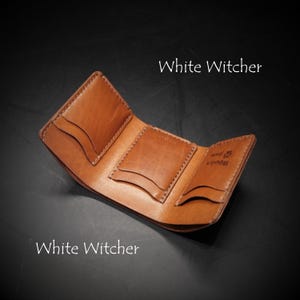 May include: A tan leather tri-fold wallet featuring three interior card slots with curved edges and visible stitching. The interior is stamped with the text 'Woolen paw' and a paw print icon. The text 'White Witcher' appears twice in the image.