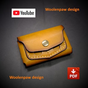 Könnte beinhalten: Ein beigefarbener Kartenhalter aus Leder mit Klappverschluss, einem einzelnen messingfarbenen Metalldruckknopf und sichtbaren gelben Nähten. Das Bild enthält den Text YouTube, PDF und Woolenpaw design in orangefarbener und weißer Schrift.