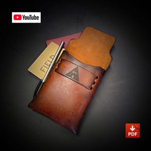 May include: A brown leather pocket organizer featuring a horizontal strap with a triangular geometric logo, a silver metal pen, and a gold-colored notebook with the text FIELD visible. The leather has a gradient finish from light to dark brown.