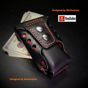 Puede incluir: Una funda de cuero negro con costuras rojas y dos botones de presión metálicos plateados. La funda presenta una serie de recortes circulares en el lateral, revelando un interior rojo. Un fajo de billetes de dólar está insertado dentro. El texto dice Designed by Woolenpaw y PDF YouTube.