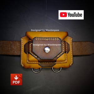 Pode incluir: Uma bolsa de cinto em couro castanho e castanho escuro com uma aba central com botão de pressão em metal prateado, costuras amarelas em contraste e dois anéis em D de metal prateado na parte inferior. O texto "Designed by Woolenpaw" está presente.
