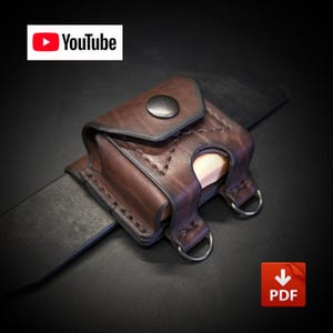 Può includere: Un marsupio da cintura in pelle marrone scuro con patta dotata di chiusura a scatto in metallo, cuciture a vista e due piccoli anelli a D in metallo sul fondo. La custodia è fissata a una cintura nera e include un logo YouTube e un'icona PDF.